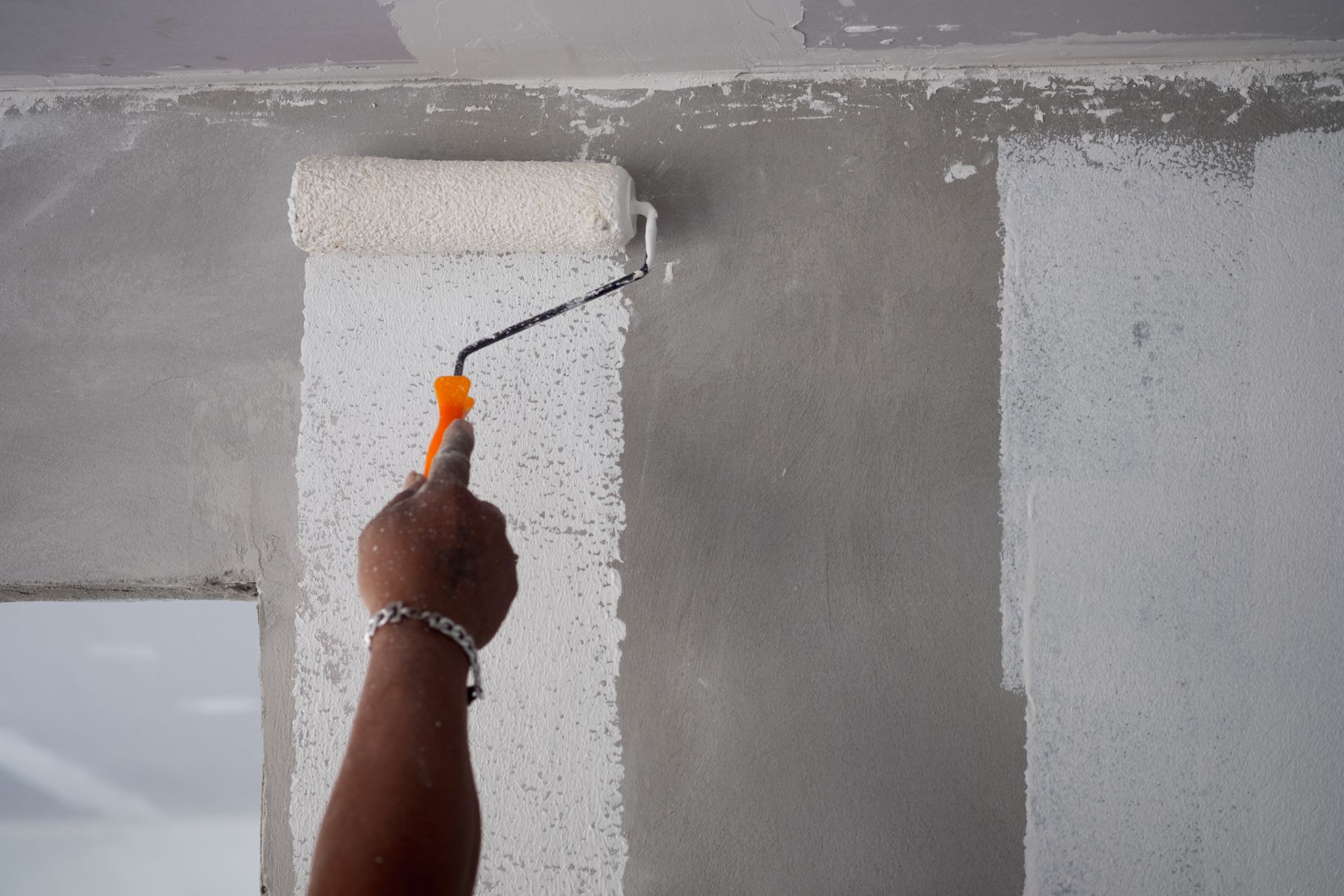 Personne utilisant un rouleau à peinture pour appliquer de la peinture blanche sur un mur texturé.