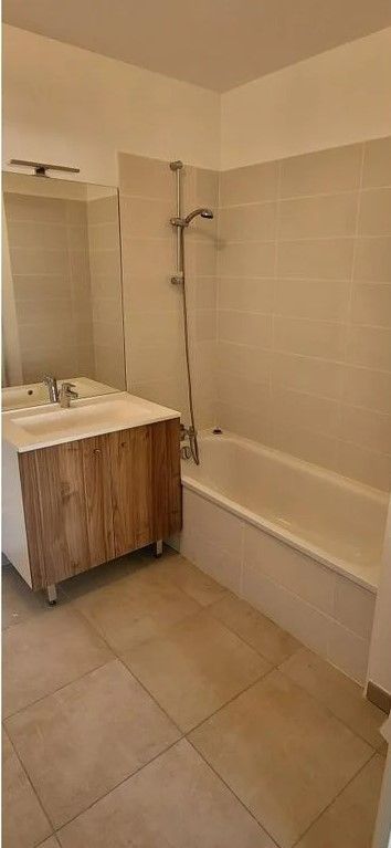 Salle de bains avec baignoire, pommeau de douche, meuble-lavabo avec armoire en bois, et carrelage au sol et aux murs.