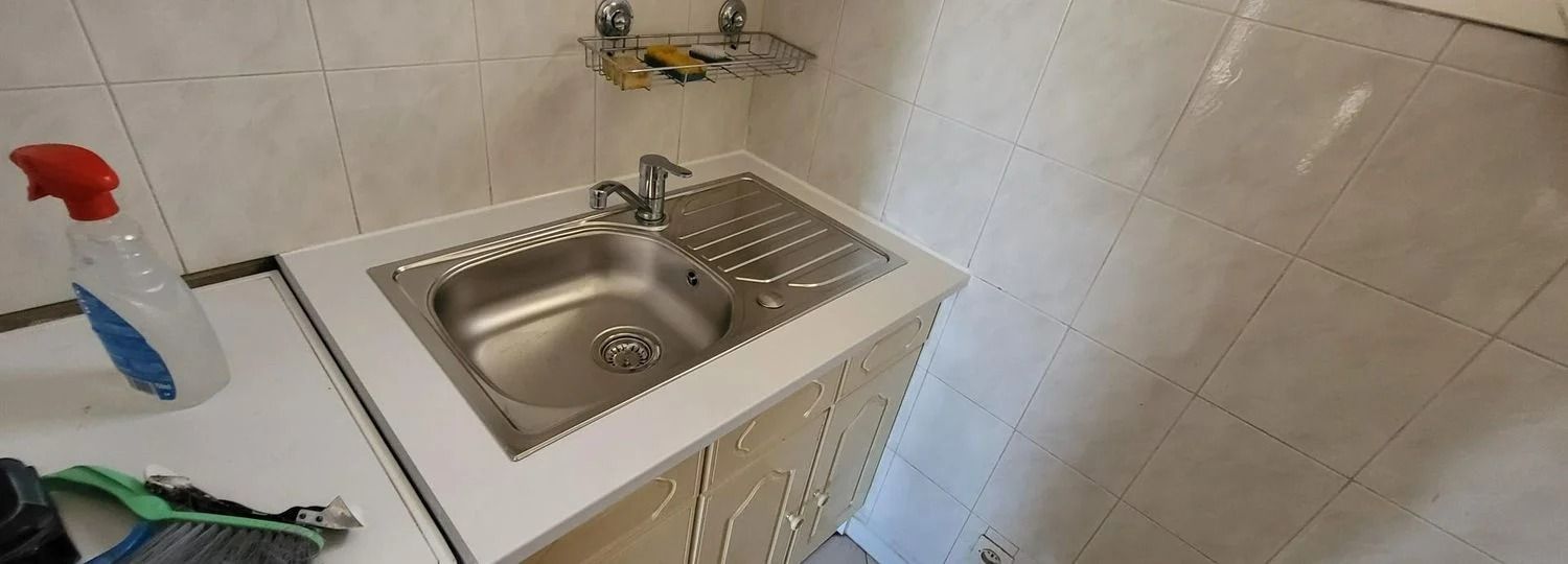 Un évier utilitaire en acier inoxydable avec un flacon pulvérisateur rouge et bleu sur le côté.