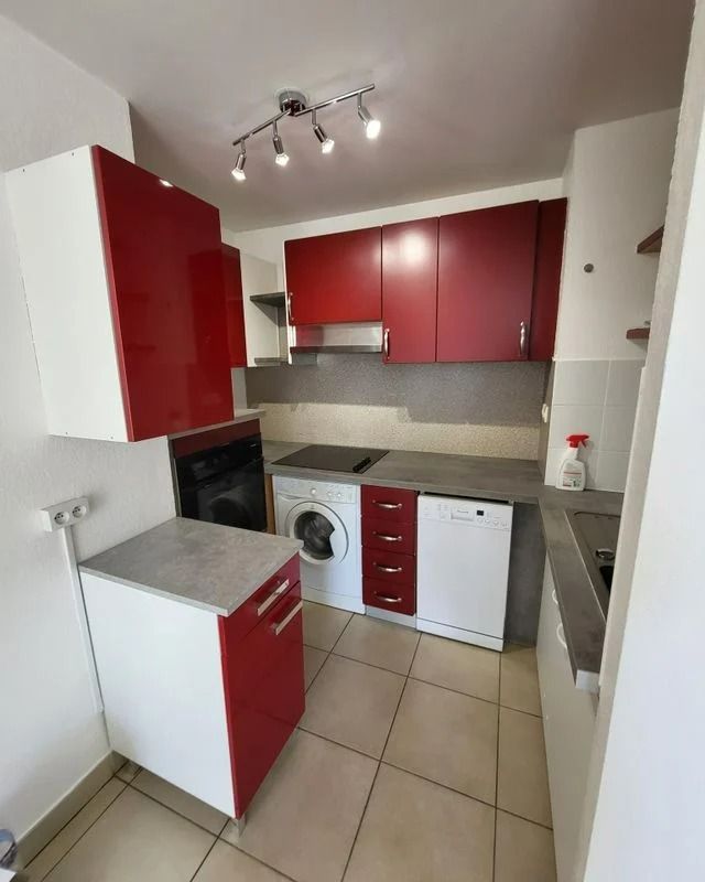 Petite cuisine avec placards rouges et blancs, appareils électroménagers et plans de travail gris.