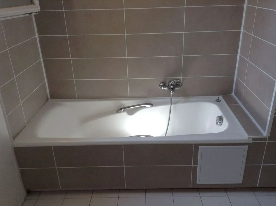 Baignoire dans une salle de bains carrelée ; baignoire blanche, robinet argenté, carrelage beige aux murs.