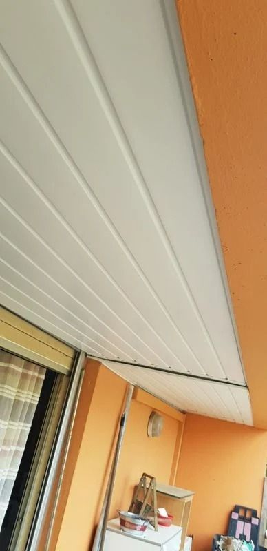 Plafond à panneaux blancs au-dessus d'un espace extérieur aux murs orange, avec un store enrouleur visible sur la gauche.
