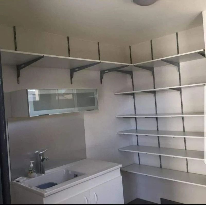 Buanderie avec étagères blanches, évier et placard suspendu.