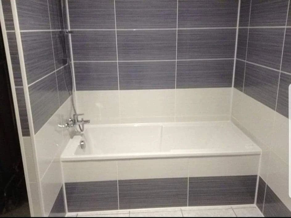 Salle de bains avec baignoire blanche et murs carrelés bicolores gris et blancs.