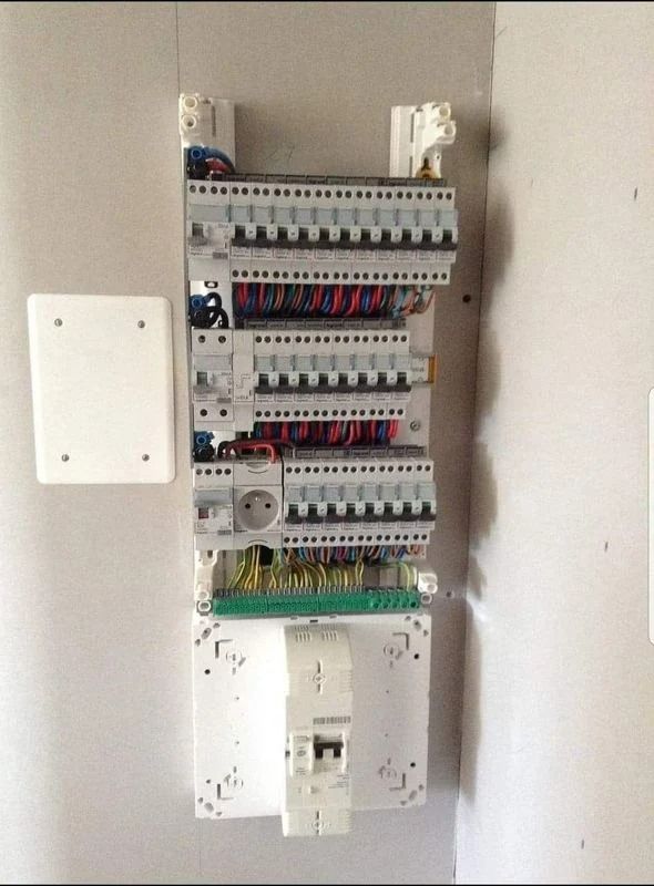 Tableau électrique avec rangées de disjoncteurs et câblage, monté sur un mur clair.