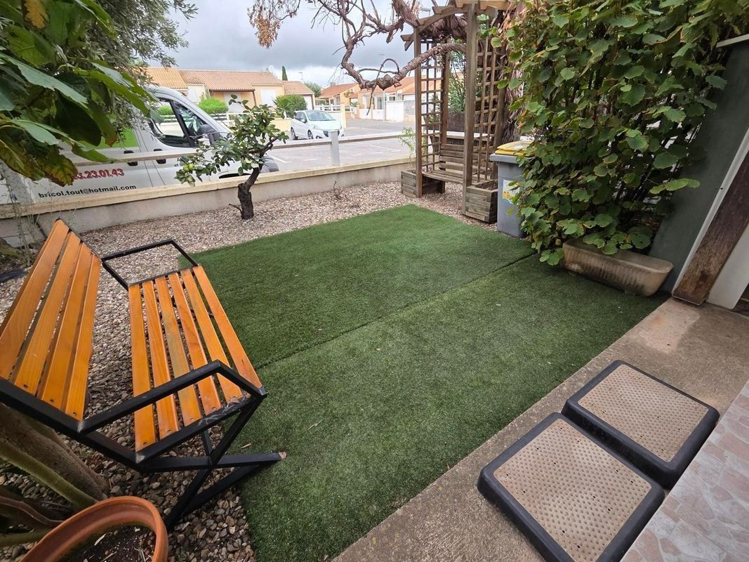 Un petit espace extérieur avec du gazon vert, un banc en bois et une treille.