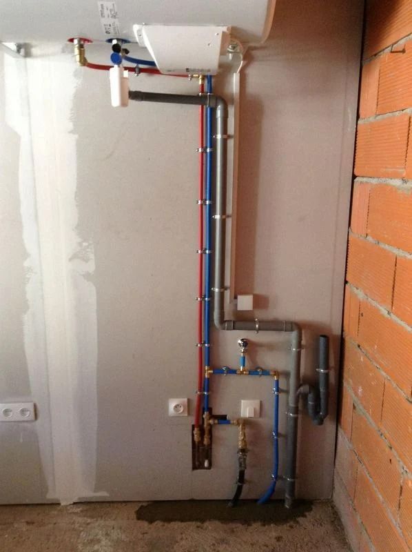 Tuyaux de plomberie contre un mur, tuyaux rouges et bleus avec raccords. Chantier inachevé.