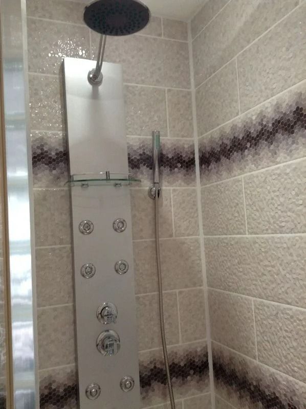 Douche avec panneau argenté, pommeau de douche de tête, jets multiples et douchette. Murs carrelés avec frise décorative.