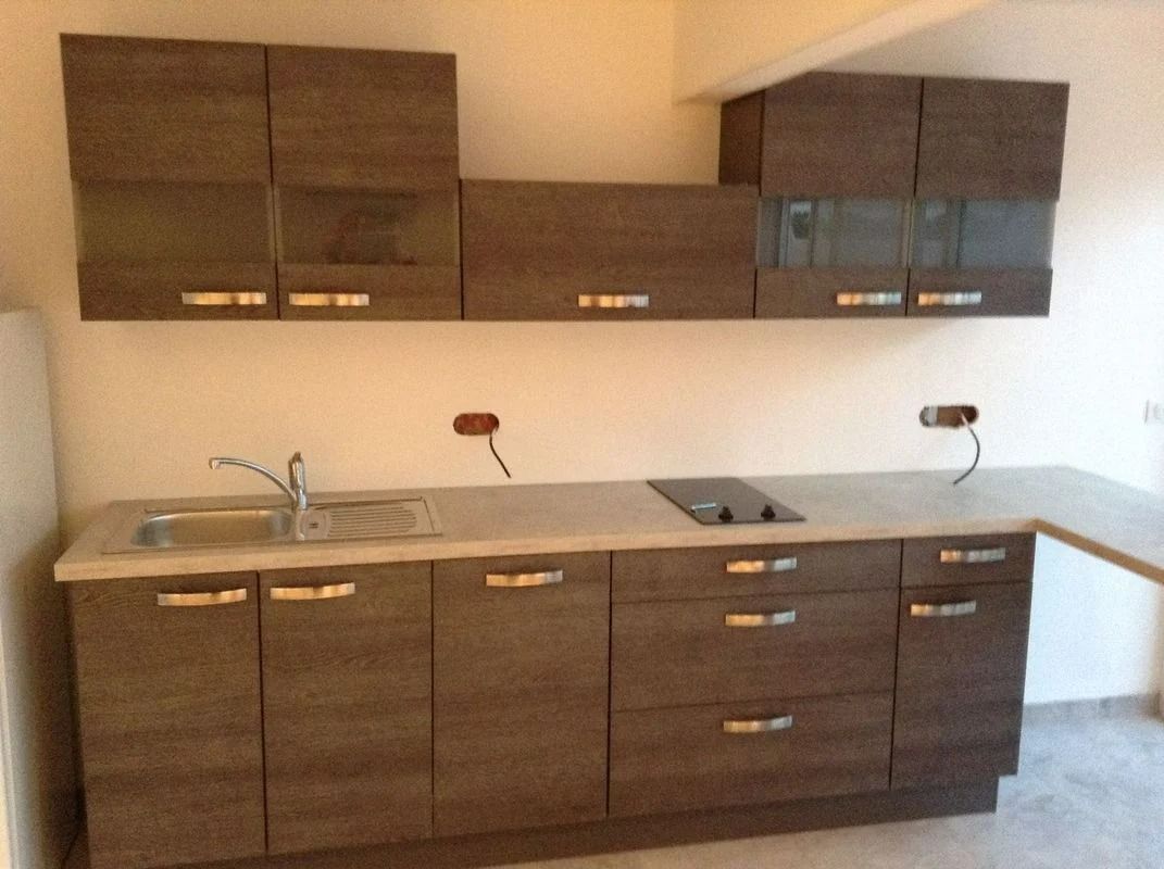 Cuisine équipée d'armoires brunes, d'un plan de travail clair et d'un évier.