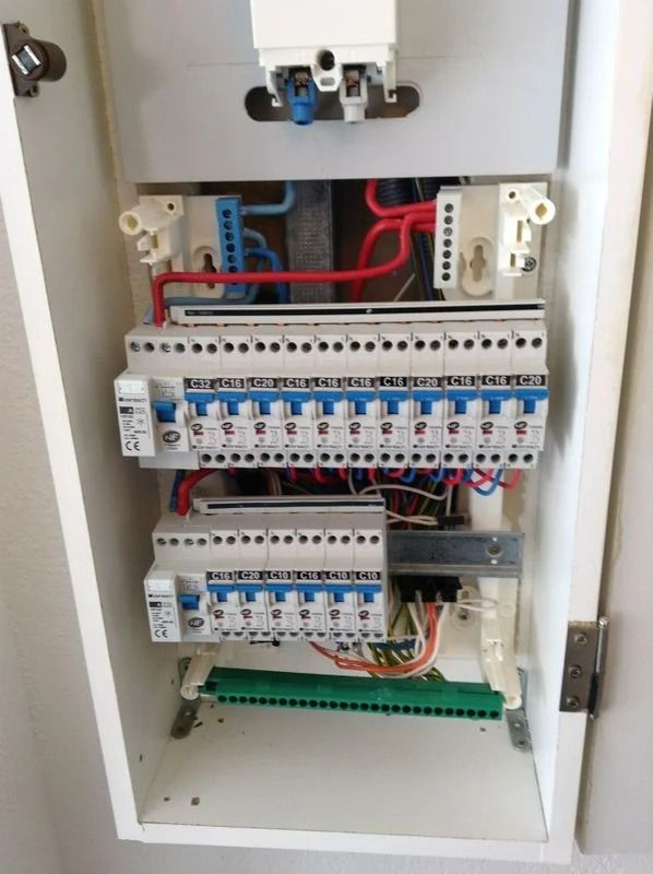 Tableau électrique avec plusieurs disjoncteurs et câblage à l'intérieur d'une armoire blanche.