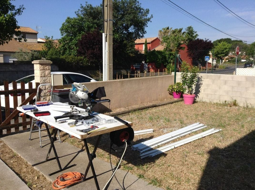 Une scie à onglets sur une table avec des moulures blanches. En extérieur, par une journée ensoleillée.