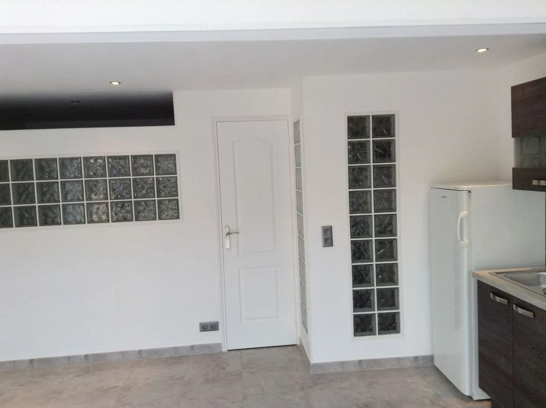 Intérieur avec une porte blanche, une fenêtre et un mur en pavés de verre, et un réfrigérateur.