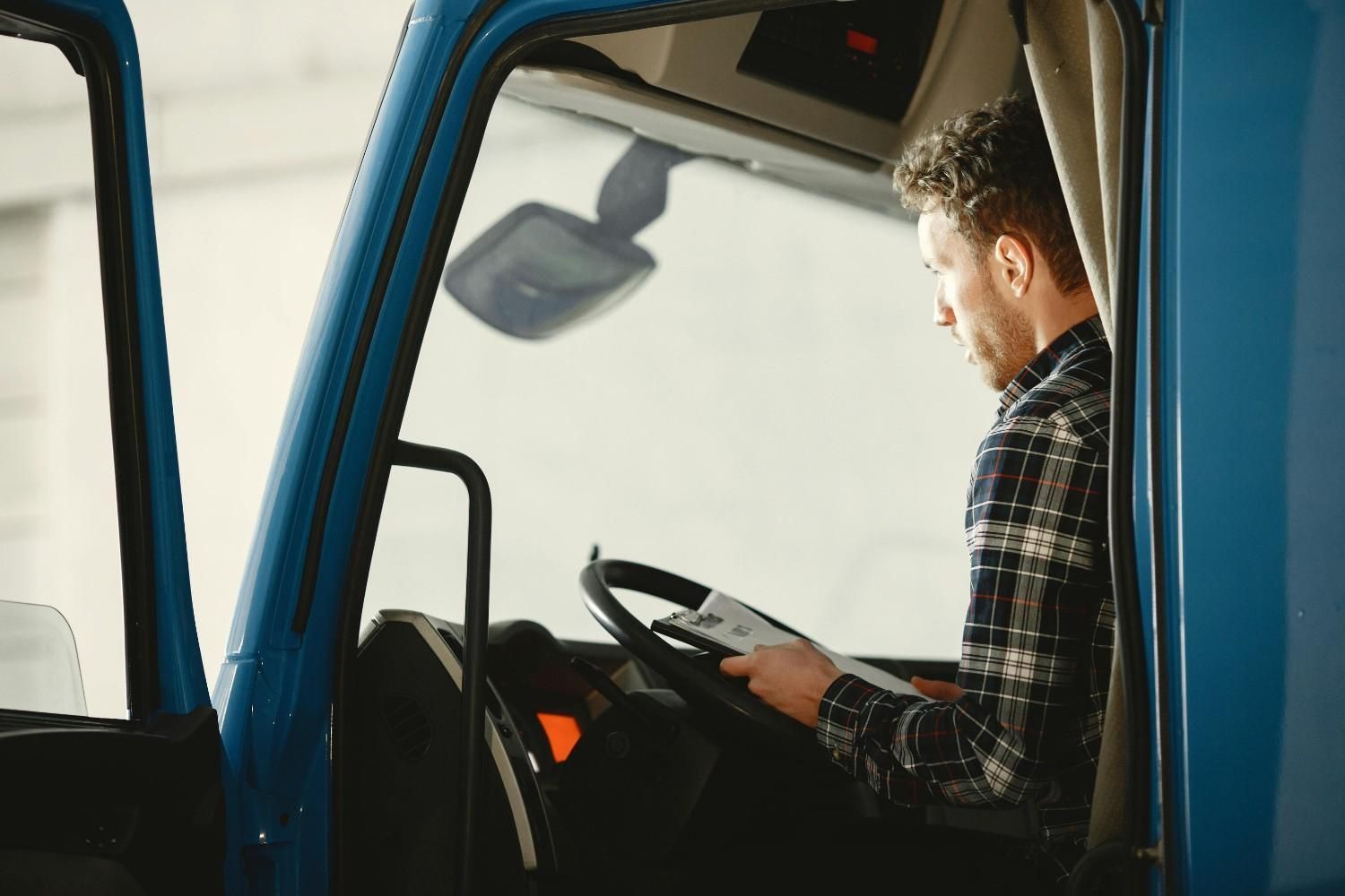 Hombre con camisa a cuadros sentado en un camión azul, mirando papeles en el volante.