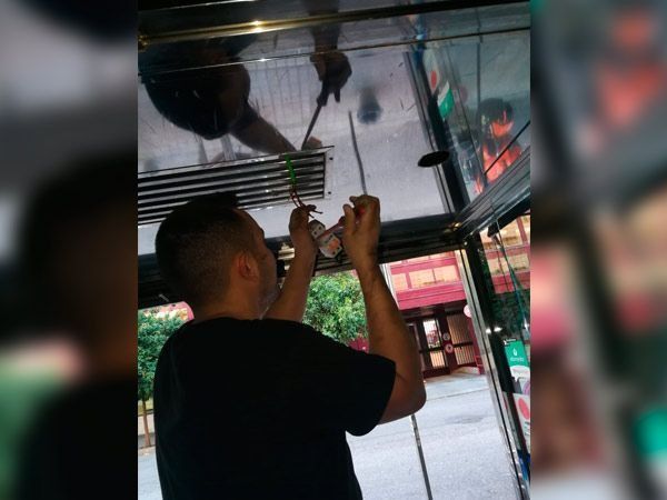 Hombre dentro de un carrito de comida, intentando reparar algo en el techo con herramientas.