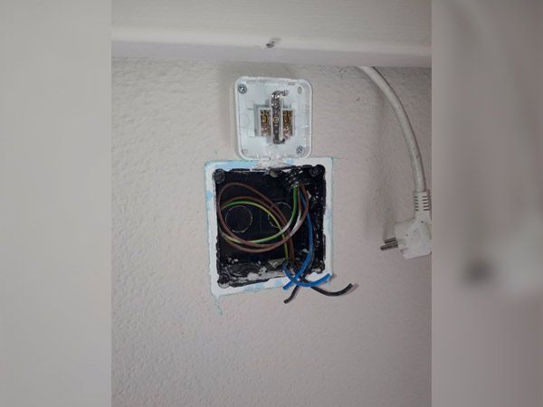 Caja eléctrica abierta con cables y una tapa de toma de corriente blanca separada en una pared.