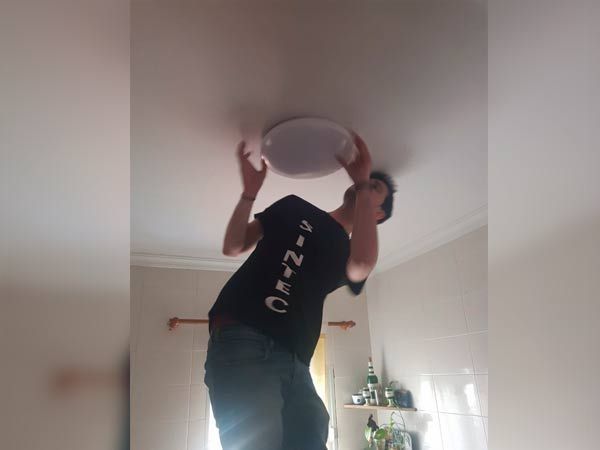 Persona en una escalera instalando una lámpara de techo en una habitación.