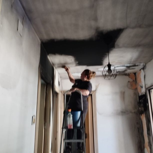 Mujer en una escalera pintando un techo ennegrecido en una habitación.