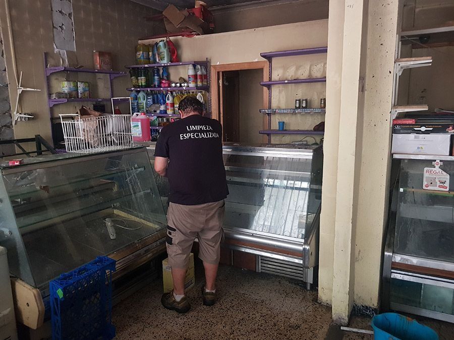 Una persona inspecciona el interior de una tienda dañada con vitrinas rotas, estanterías y escombros.