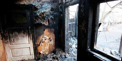 Habitación interior gravemente dañada por el fuego; paredes, puerta y ventana carbonizadas. Escombros en el suelo.