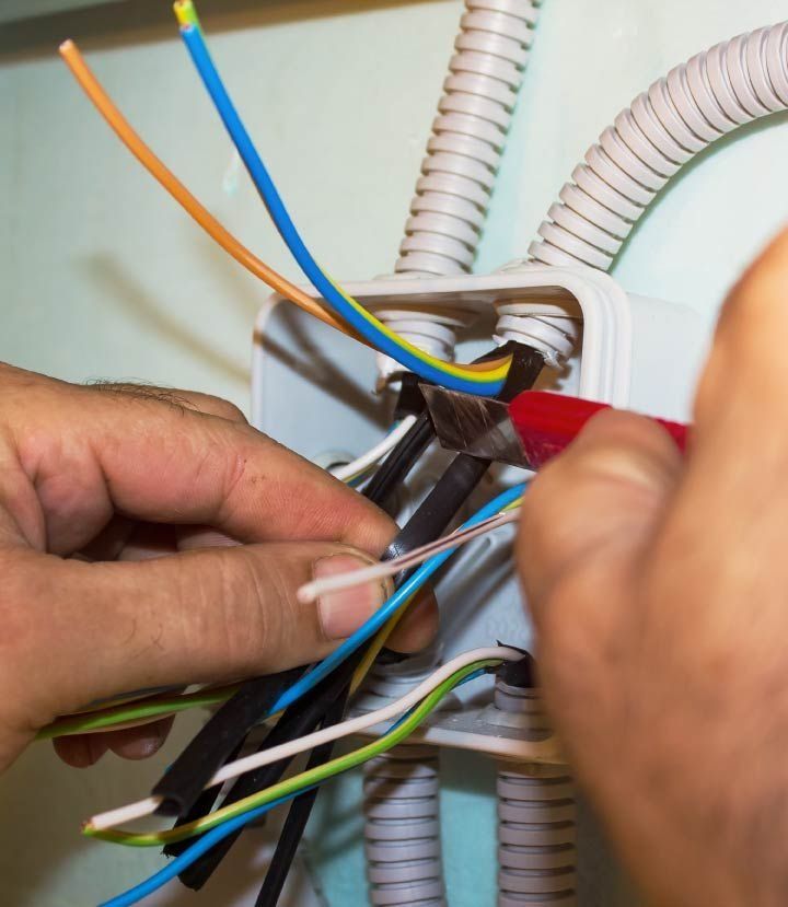 Manos cableando caja eléctrica, con cables de colores, utilizando alicates.