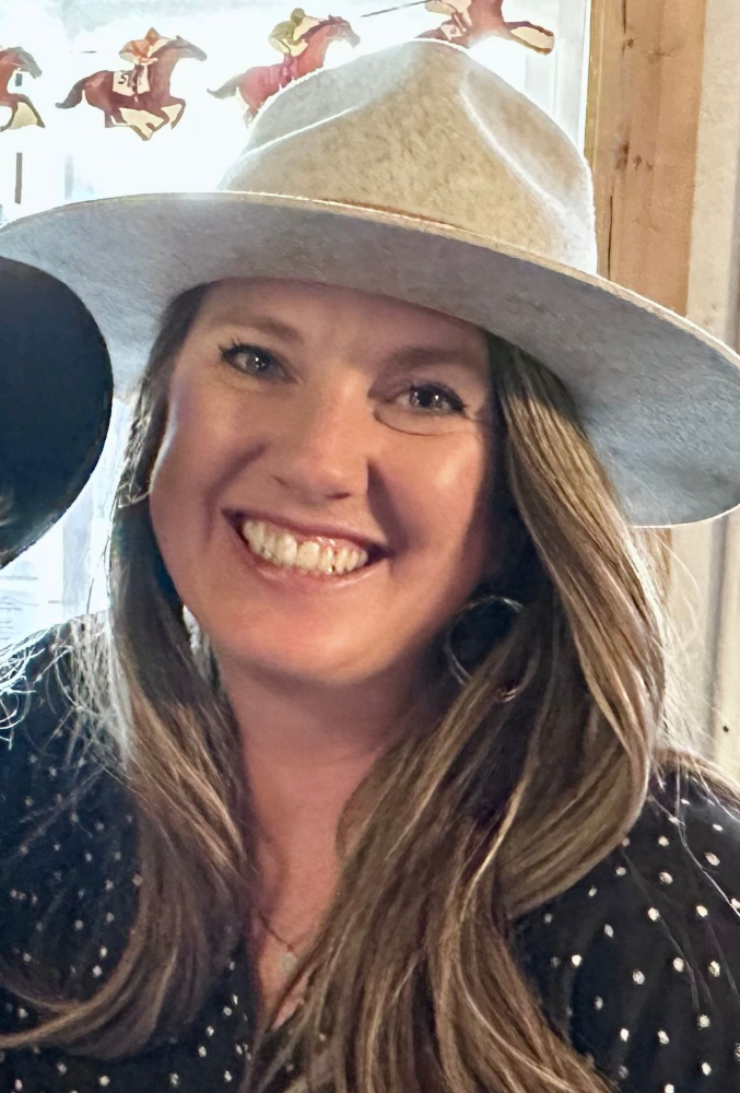 A man is standing next to a red fence in front of a herd of cows.