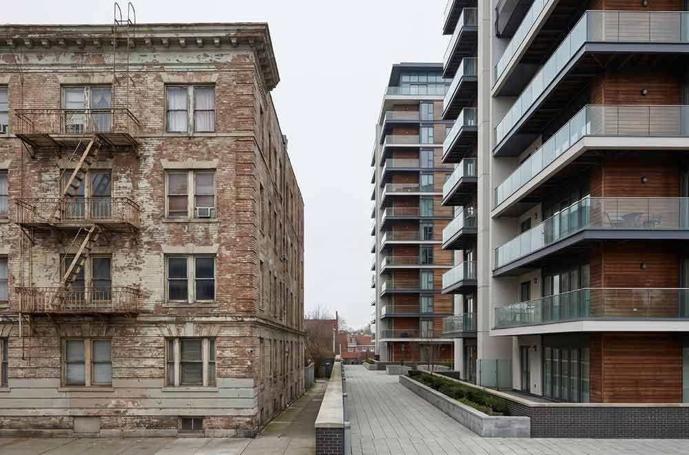 Altes Steingebäude neben modernen Wohnungen entlang eines gepflasterten Gehwegs an einem bewölkten Tag