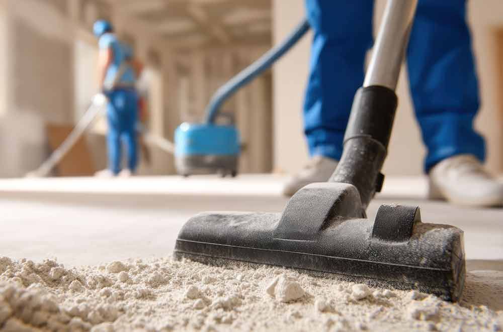 Teppichreinigung im Gange; im Hintergrund ist ein Staubsaugeraufsatz auf einem hellen Boden und Arbeiter zu sehen.
