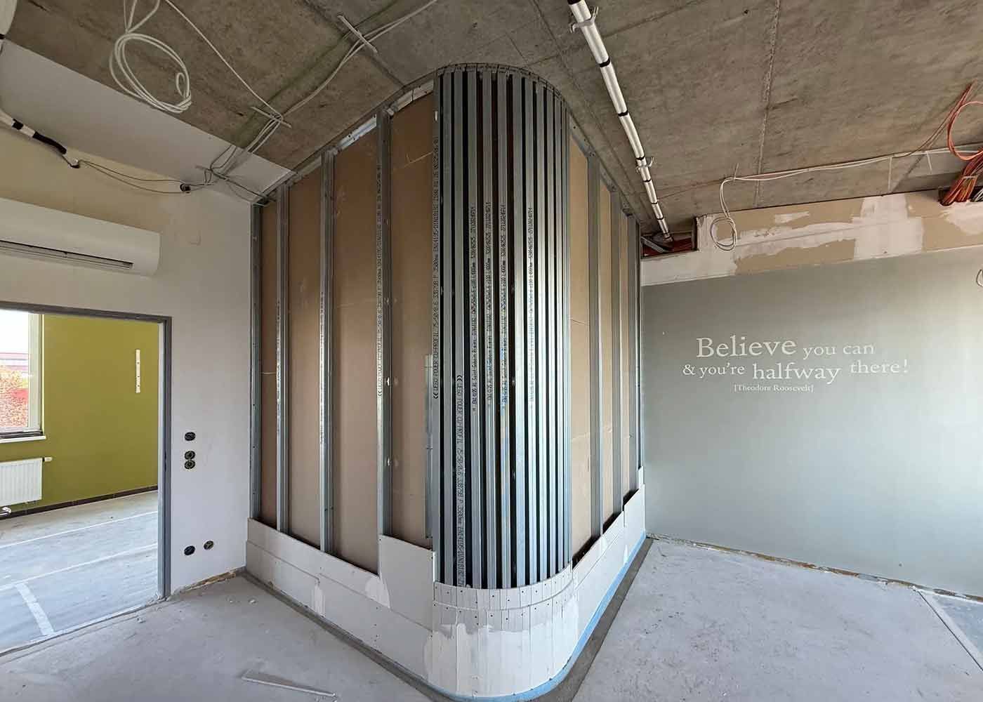 Leeres, modernes Interieur mit Sichtbeton, geschwungener Lamellenwand und Wandtext mit der Aufschrift „Believe in the...“