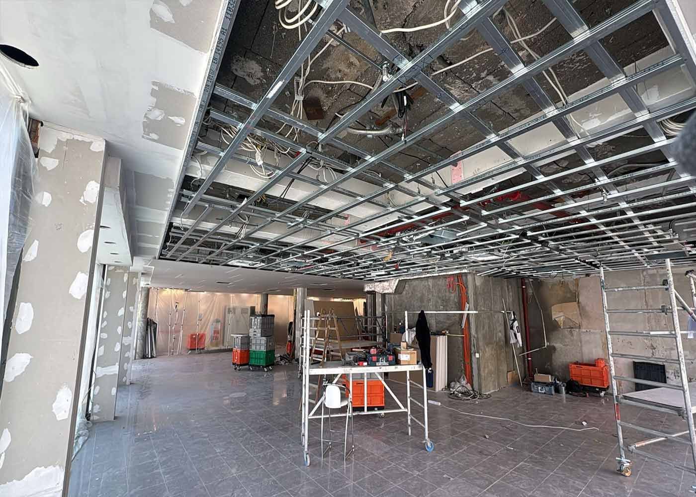 Renovierungsbaustelle mit freiliegender Deckenkonstruktion, Gipskartonwänden, Gerüst und Baumaterialien in einem großen Raum