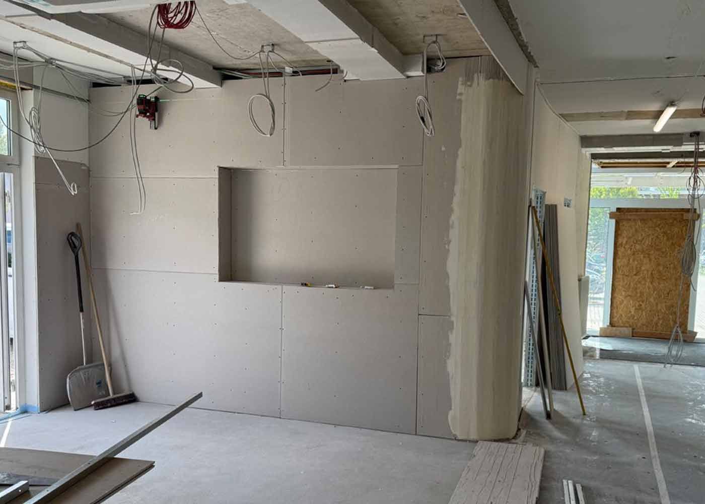 Innenausbaustelle mit unfertigen weißen Wänden, freiliegenden Deckenbalken und einer Fensteröffnung