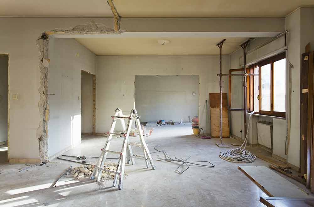 Renovierungsraum mit Leitern, Werkzeugen und freiliegenden Wänden und Fenstern, die auf dem Boden verstreut liegen.