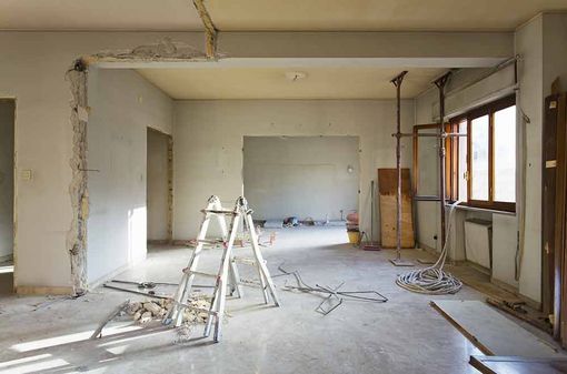 Renovierungsraum mit Leitern, unverputzten Wänden, Werkzeugen und unfertigem Fußboden in Fensternähe