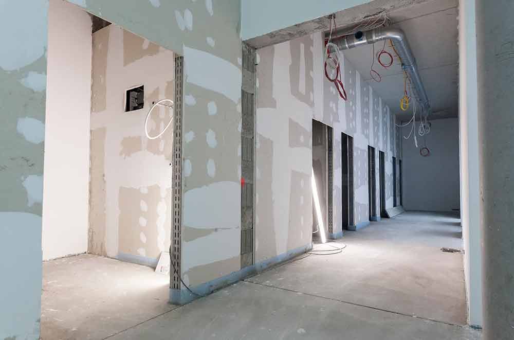 Unfertiger Flur mit Trockenbauwänden, freiliegenden Kabeln und offenen Türen in einem im Bau befindlichen Gebäude