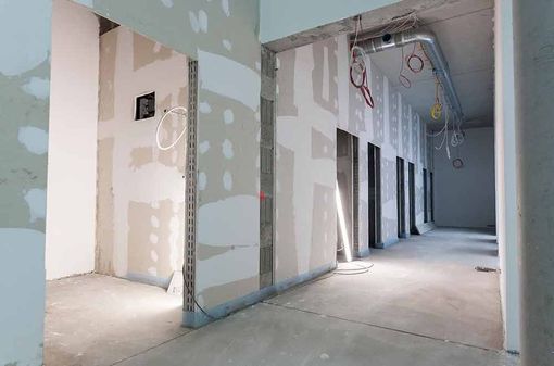 Unfertiger Innenkorridor mit Gipskartonplatten, freiliegenden Kabeln und Betonboden in einem im Bau befindlichen Gebäude