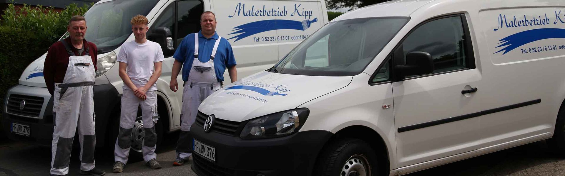 Drei Männer stehen vor zwei weißen Lieferwagen.