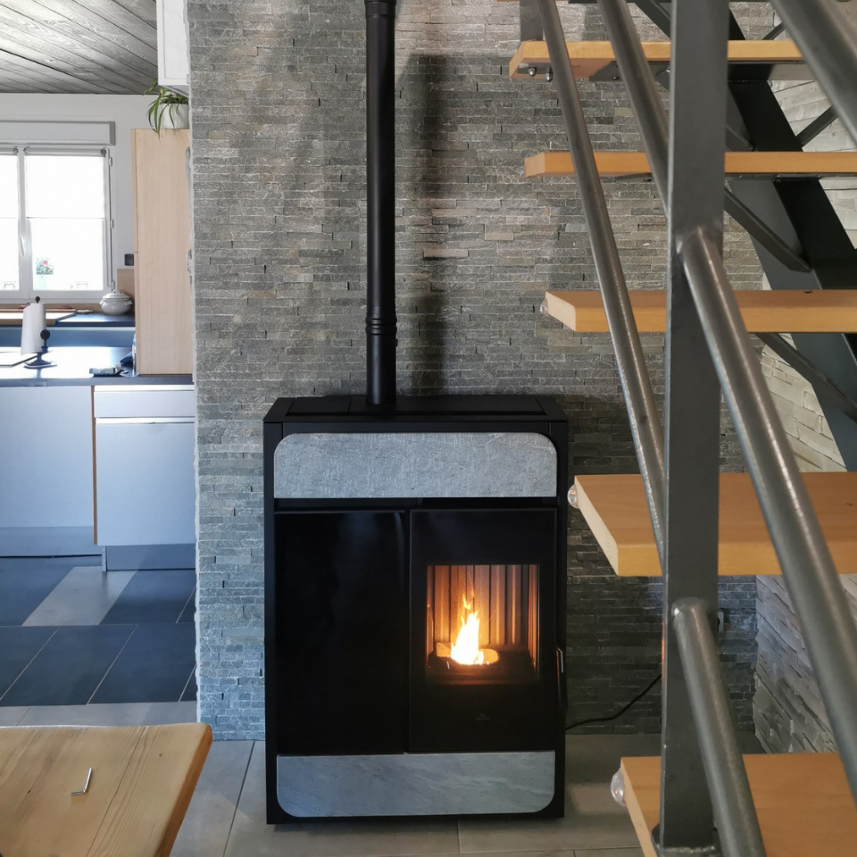 Un poêle noir est posé devant un mur de pierre