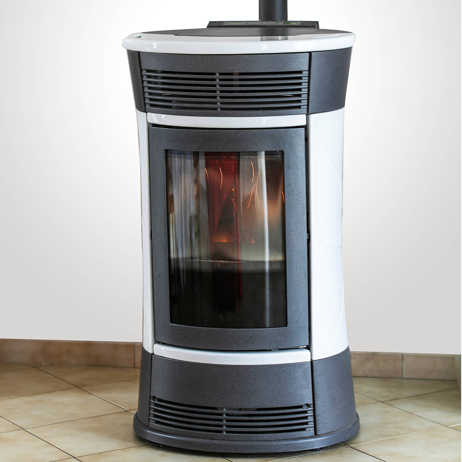Un poêle blanc avec une porte vitrée est posé sur un sol carrelé.