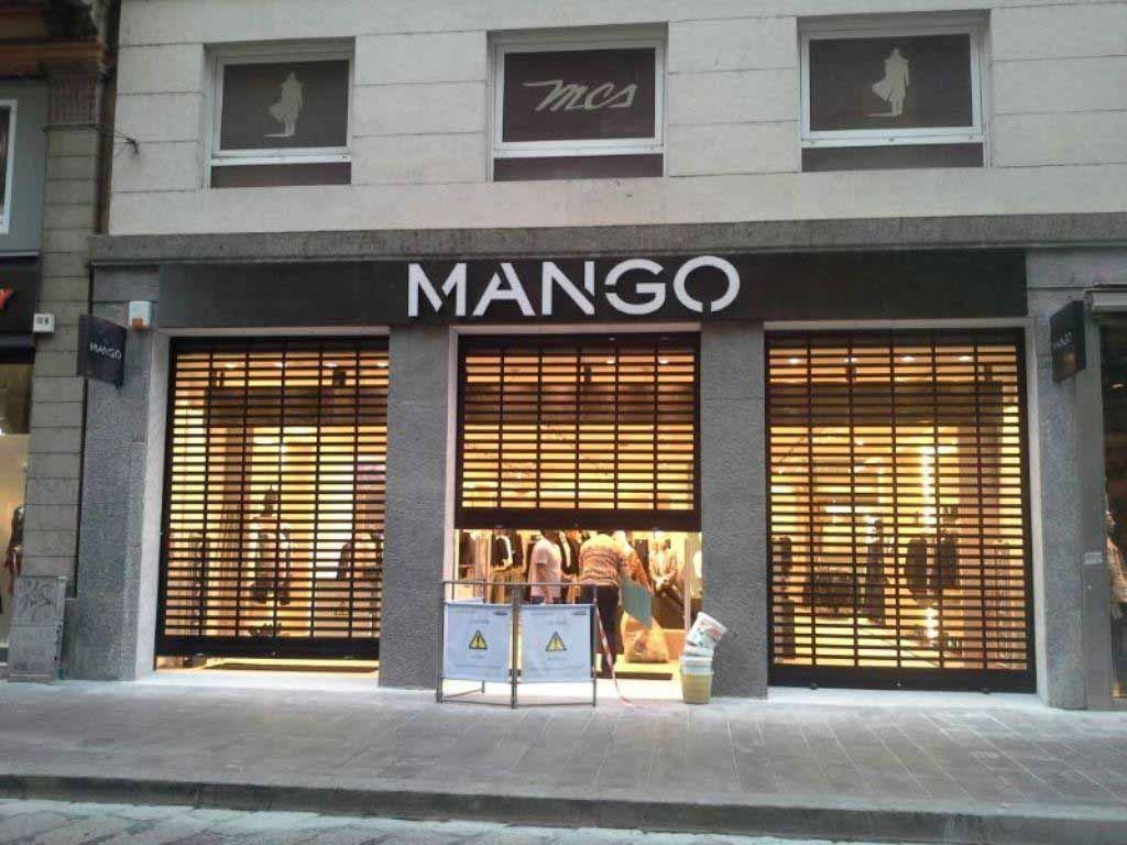 Tienda de ropa Mango con persianas de seguridad cerradas; fachada del edificio.