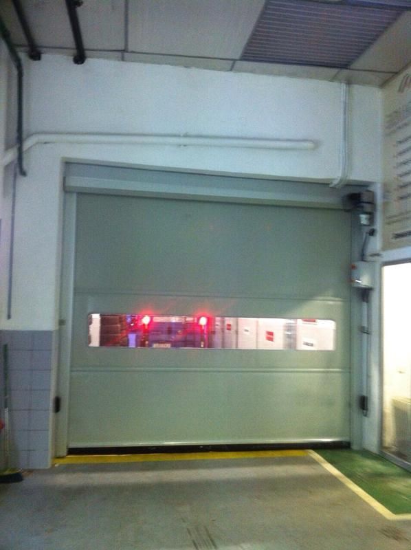 Puerta enrollable industrial cerrada con ventana y luces rojas. Vista interior.