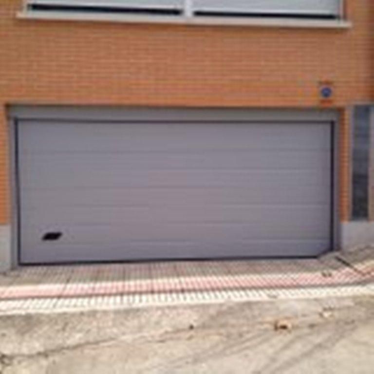 Puerta de garaje gris en la fachada de un edificio de ladrillo.