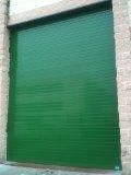 Puerta enrollable verde y cerrada en un edificio de ladrillo.