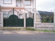 Puerta y valla de metal verde con un edificio blanco al fondo.