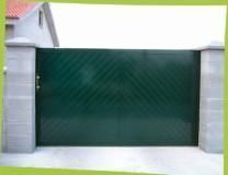 Portón metálico de color verde con dibujo diagonal entre dos pilares de hormigón, frente a una casa.