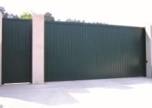 Puerta corredera verde oscuro y puerta peatonal entre pilares de hormigón.