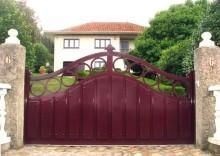 Puerta de metal de color burdeos delante de una casa blanca con techo naranja.