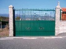 Puerta verde con herrajes, entre pilares de piedra y con las montañas como telón de fondo.