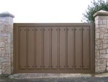 Puerta metálica de color marrón con paneles verticales dispuestos entre pilares de piedra.