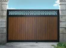 Puerta de madera marrón con borde negro y detalle decorativo superior, colocada entre pilares de piedra.