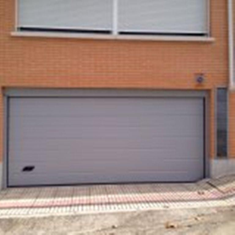 Puerta de garaje gris en fachada de edificio de ladrillo, con ventana encima.
