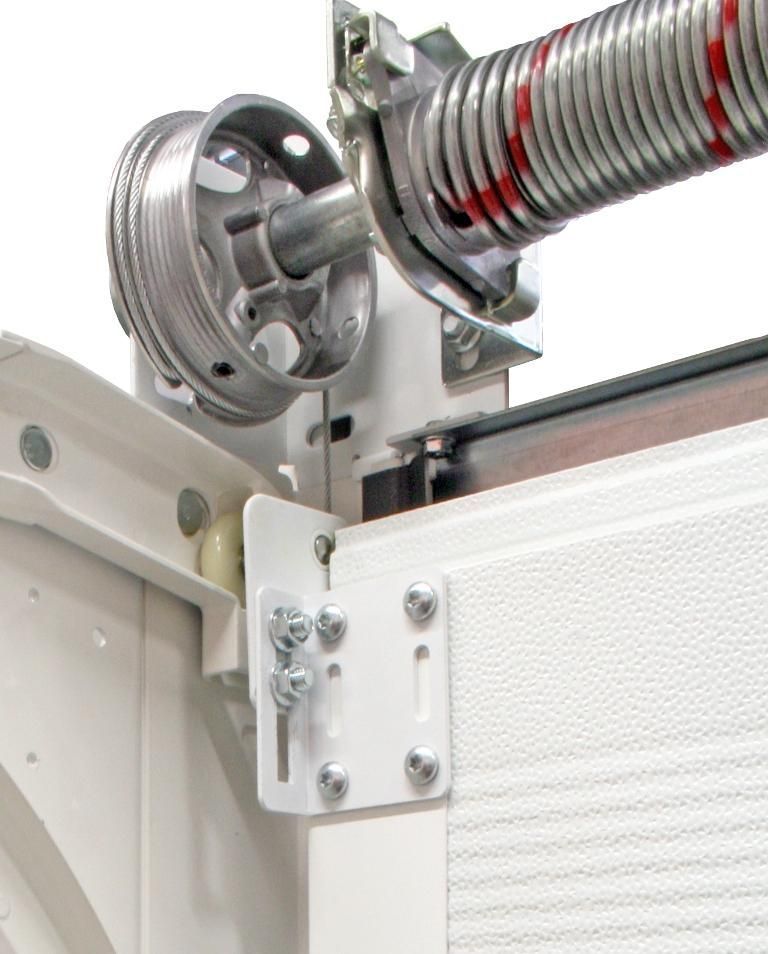 Sistema de resorte y polea para puerta de garaje, montado en un marco blanco. Se ve un resorte con rayas rojas.